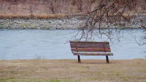 Banco-De-Madera-Junto-Al-Río-En-Movimiento-Y-Ramas-De-árboles-En-Invierno-Cerca-Del-Parque-De-La-Ciudad-Cueva-Uplistsikhe-En-Georgia