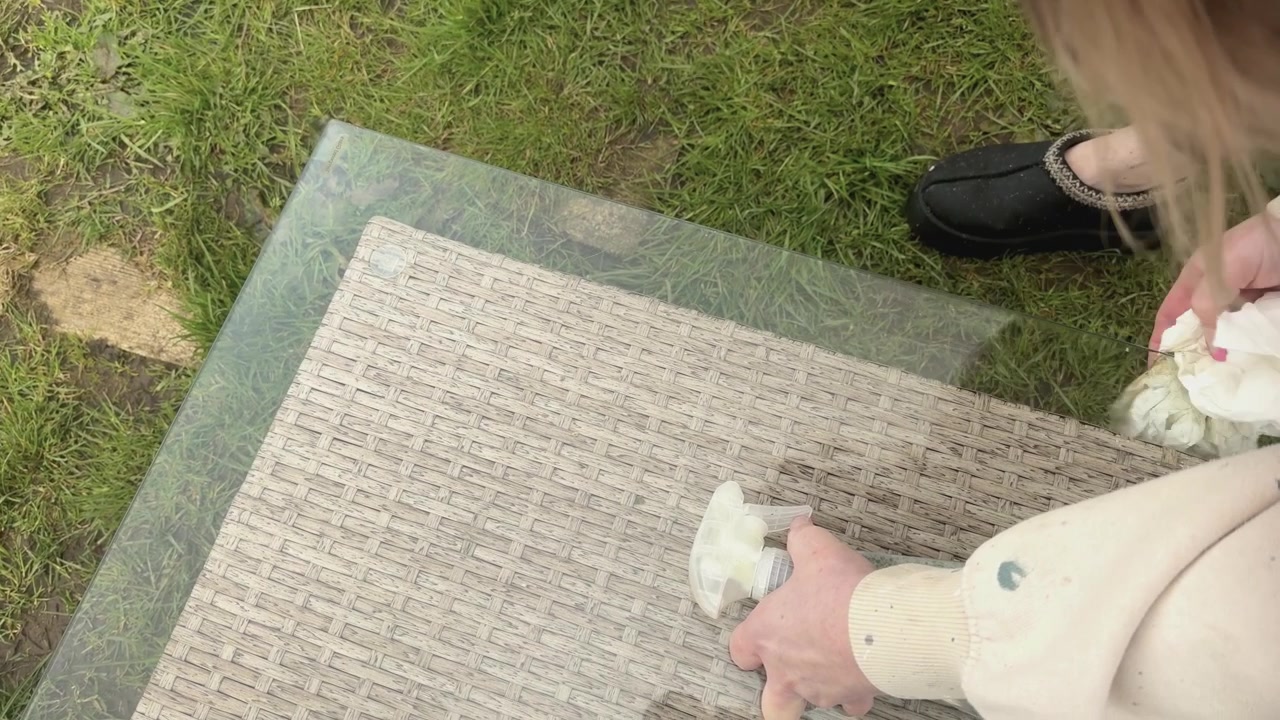 Person tørrer og rengør et havebord med glasplade udendørs. Velegnet til koncepter inden for husarbejde, rengøring, hygiejne og vedligeholdelse af hjemmet, nærbillede set oppefra.