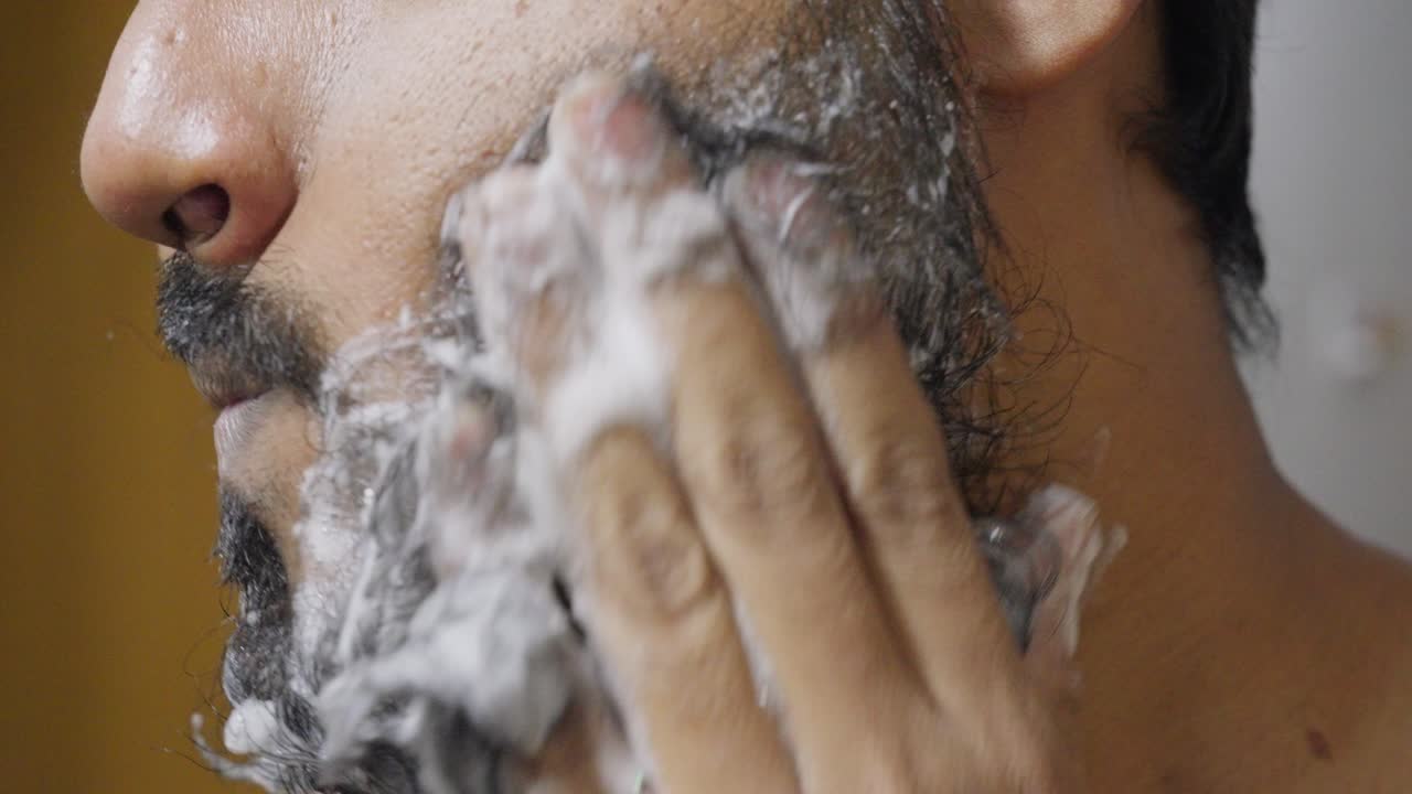 A close-up footage of a South Asian man rubbing his beard with soap and water, with a blurred background