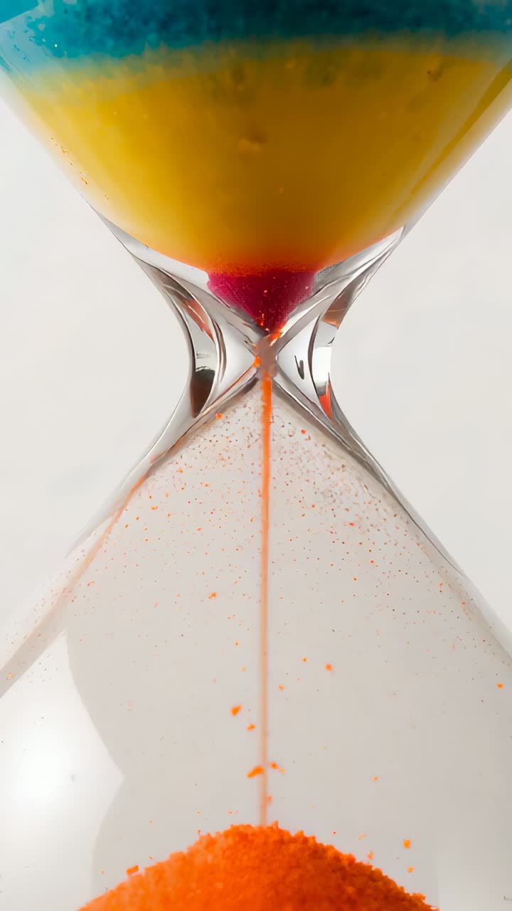 Vertical video: Pouring hourglass sending orange sand from red throat at studio showing blue yellow