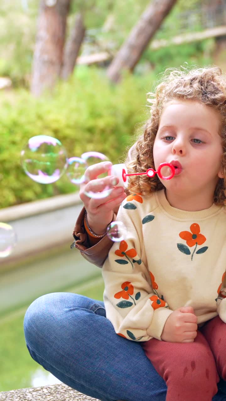 Child blowing bubbles with parent outdoors