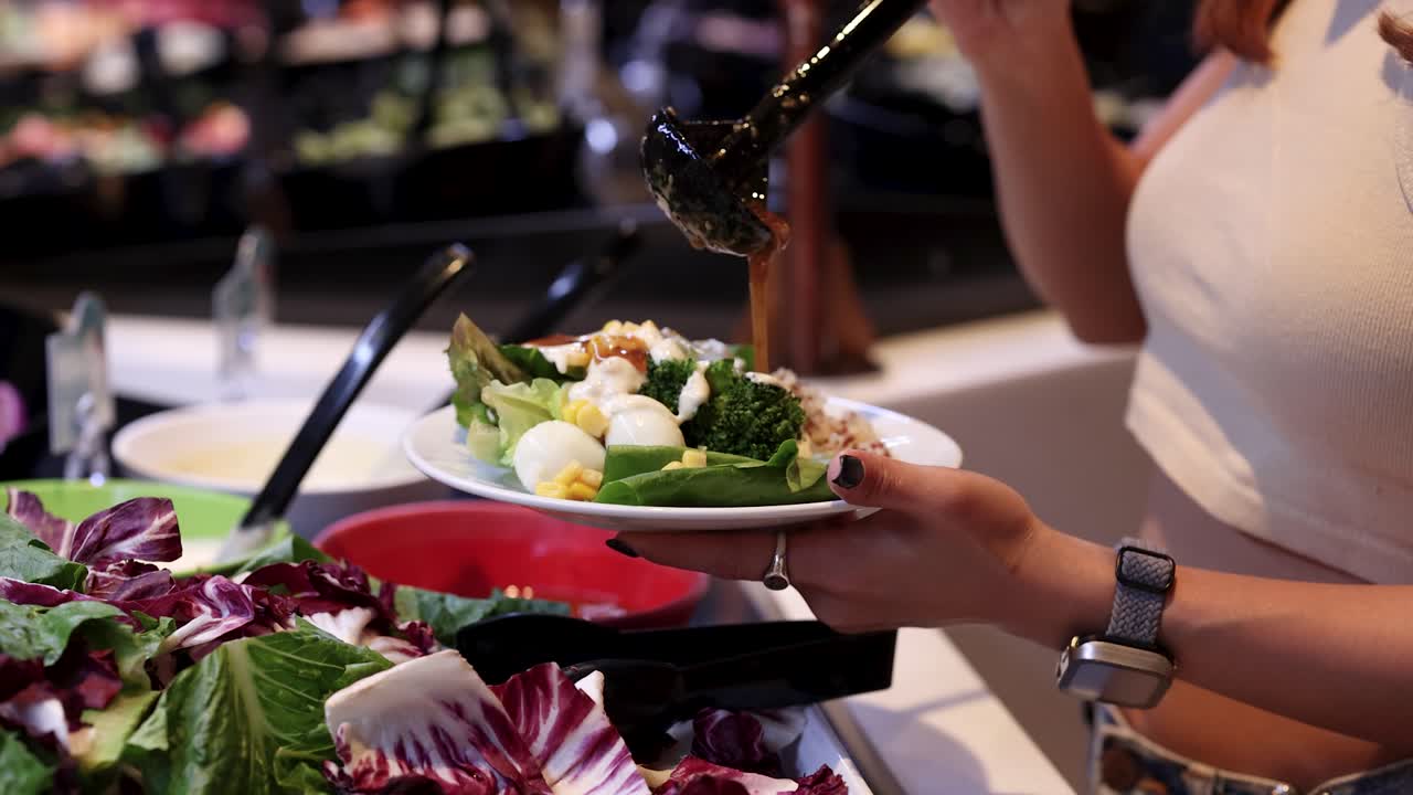 Close-up of woman adding dressing to mixed greens salad at self-serve salad bar, indoor lighting