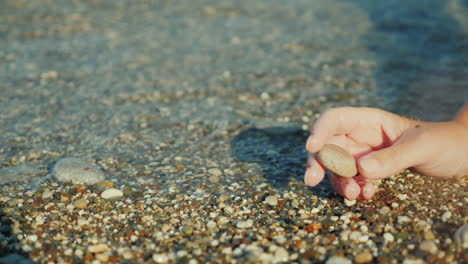 a woman's hand holds a pebble against the background of the surf 4k video