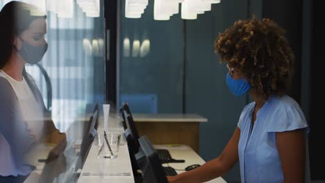 mixed race woman and female receptionist wearing face masks at hotel reception desk