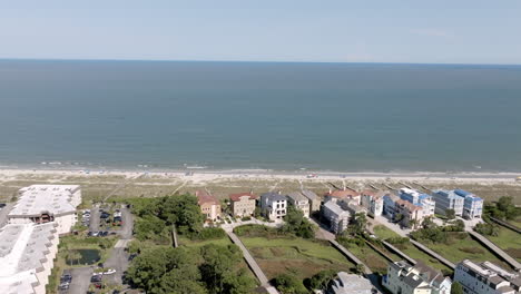 wide aerial shot of the hilton head coastline with rows of beach houses and condos facing the calm atlantic. the ocean horizon stretches far beyond the residential beachfront