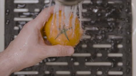 A Caucasian male is washing and rinsing a tomato in a home kitchen