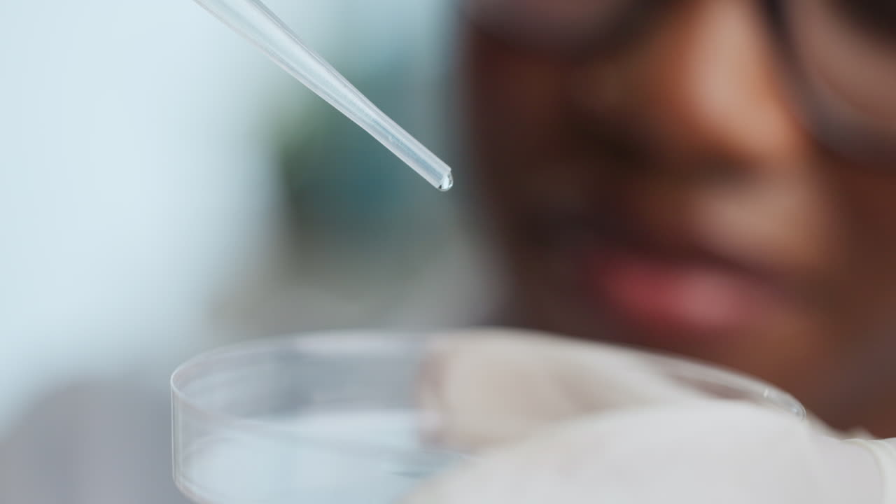 A scientist using a pipette to transfer a droplet into a petri dish in a lab