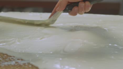 Close-up-of-a-worker-spreading-out-icing-on-a-large-slab-of-cake-and-then-decorates-with-a-line-pattern