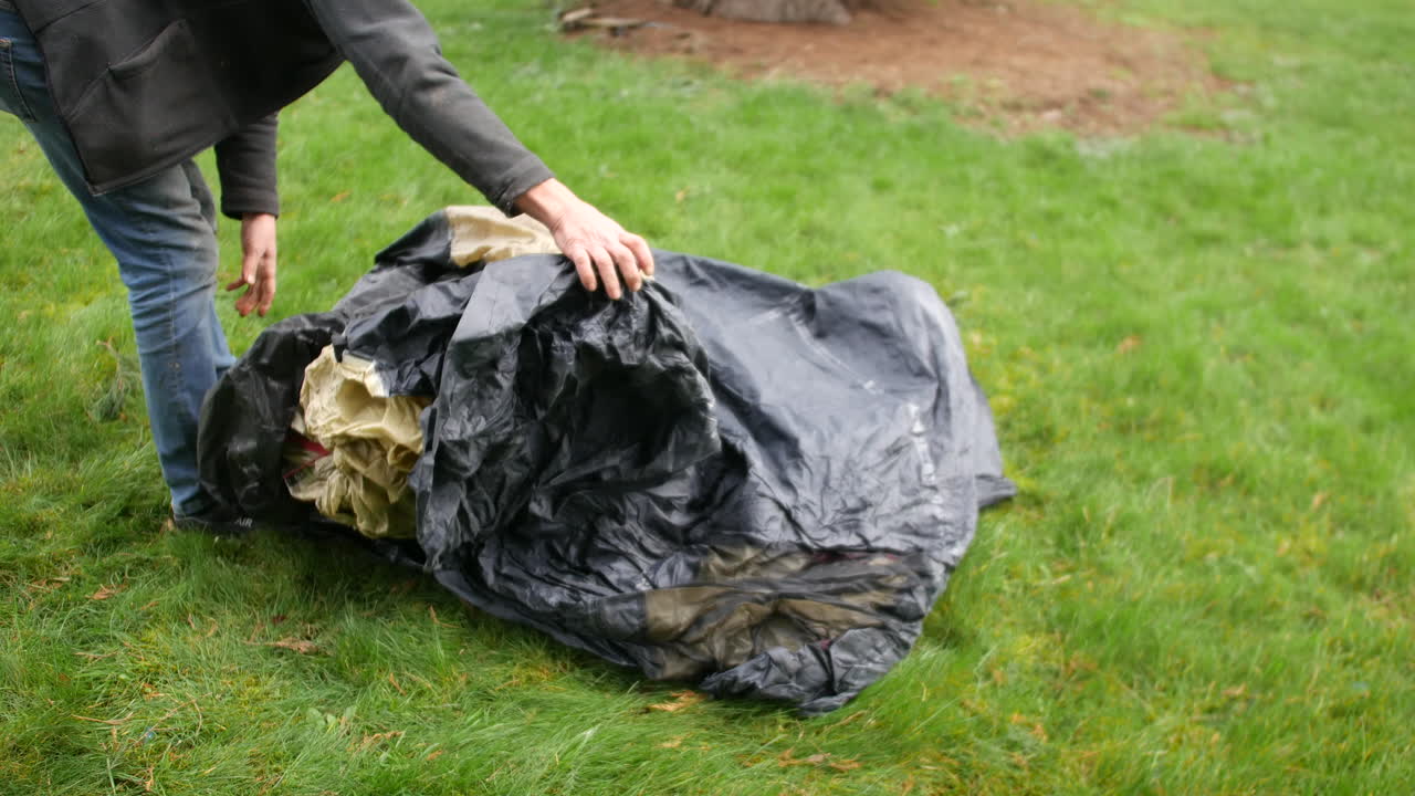 Un uomo maturo che monta una tenda a terra in un campeggio mentre si accampa in un campo sull'erba