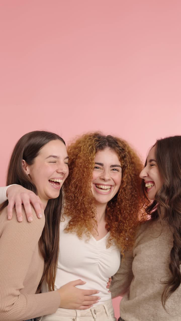 Three young women laughing together on pink background