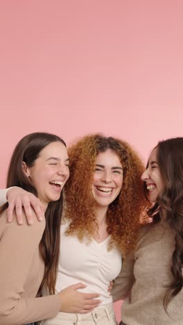 three young women laughing together on pink background