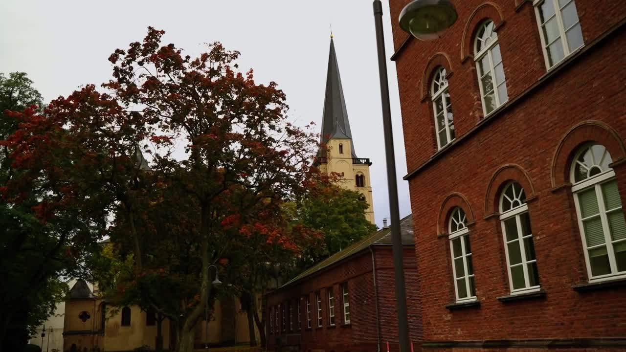 Torre della chiesa del monastero di Maria im Kapitol tra case e alberi in lontananza, in primo piano vecchi mattoni e alberi