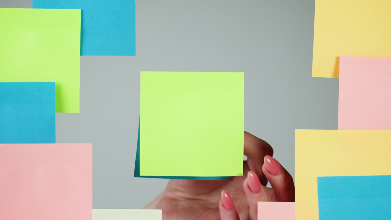 Mano che rimuove un post-it verde vuoto da uno sfondo grigio