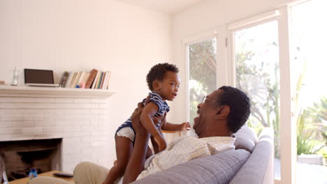 Grandfather-And-Grandson-Playing-Game-On-Sofa-At-Home