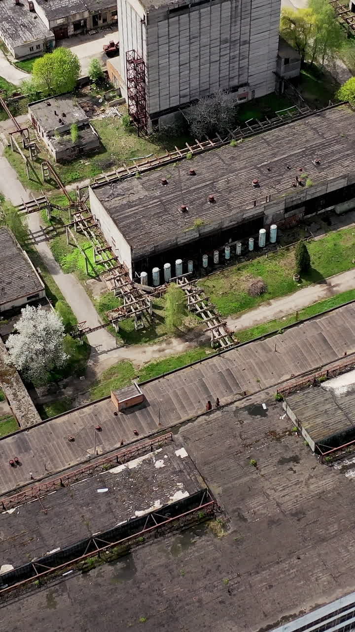 Rusty destroyed roofs of abandoned factory buildings. Empty ruined territory of a factory in spring. Aerial view. Vertical video