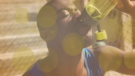 yellow spots of light against close up of african american fit man drinking water