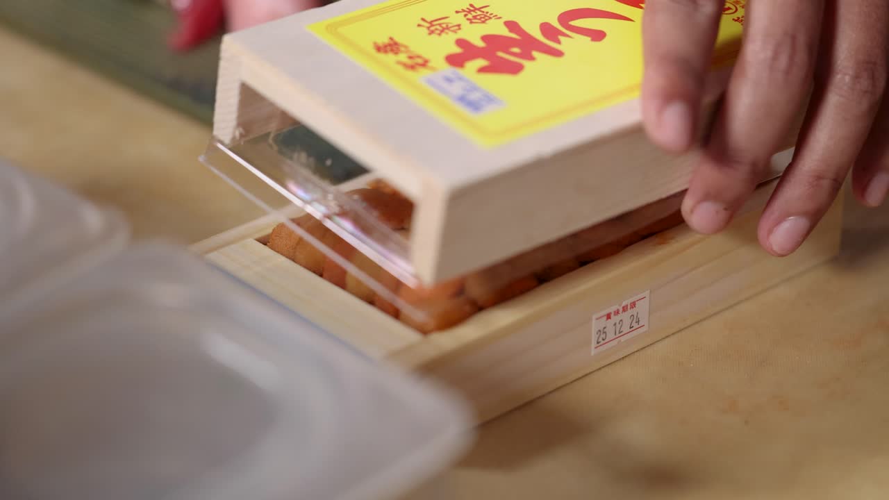 Close-up shot of hands closing a traditional wooden box containing fresh Japanese sea urchin