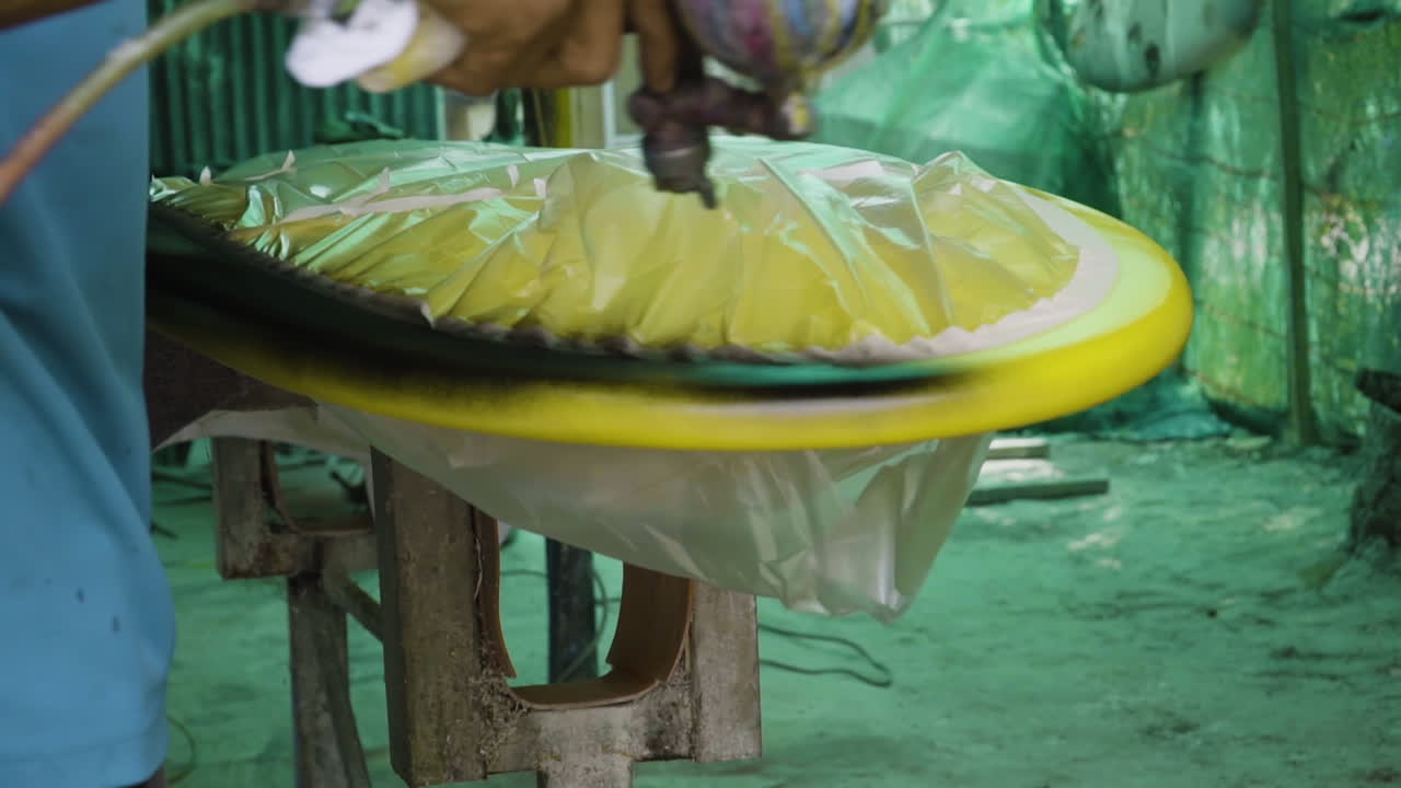 Artist sprays black paint on edge of surfboard to finish his design