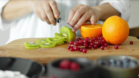 mujer joven cortando kiwis en una tabla de cortar de cocina