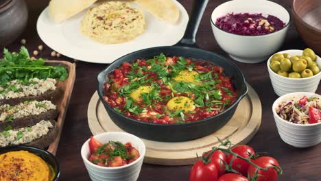 traditional israeli cuisine. shakshuka in pan decorated with parsley, forshmak and hummus on table. national jewish dishes. eggs fried in tomato sauce, dip, pita, middle eastern culture