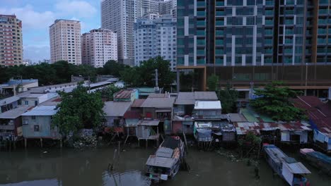 Vista-Aérea-Del-Canal-Kenh-Te-De-La-Ciudad-De-Ho-Chi-Minh-Con-Antiguas-Chozas-De-Hierro-Y-Madera,-Barcos-Fluviales-Tradicionales-Y-Edificios-Ultramodernos-De-Gran-Altura-En-Un-Día-Soleado