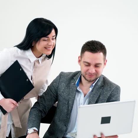 happy young couple in the studio background. handsome businessman sitting with a laptop and smiling girl secretary standing nearby.