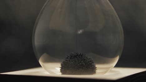 detailed shot of iron filings form a spiky, textured mound inside an hourglass, reacting to magnetic forces