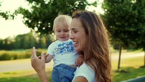 Mother-holding-son-on-hands-in-park.-Woman-and-toddler-playing-with-soap-bubbles