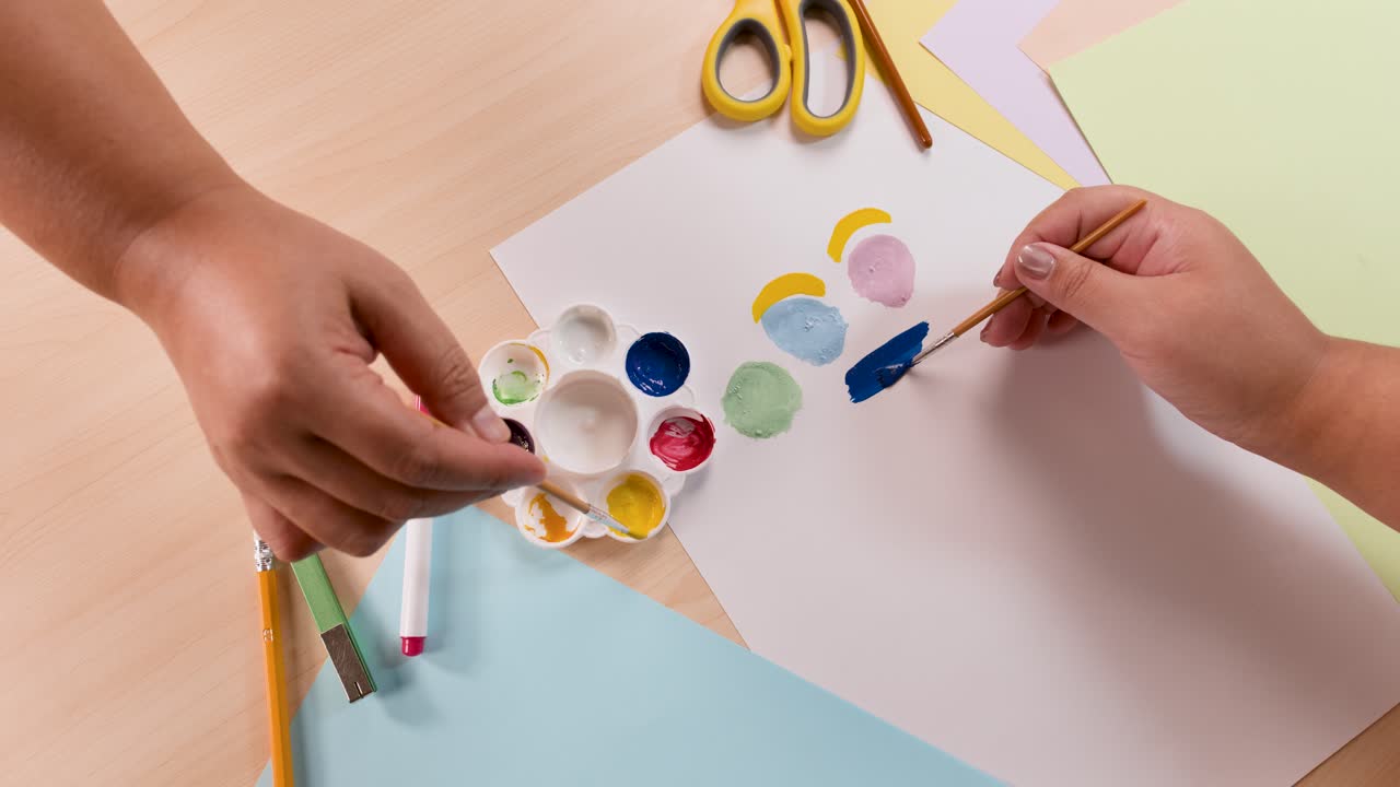 Children’s hands painting with brushes on paper, using colorful palette, under bright even lighting