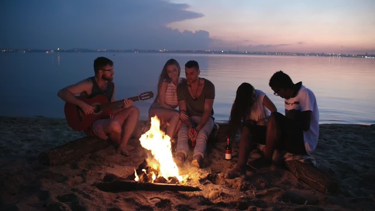 Giovani seduti intorno a un fuoco sulla spiaggia