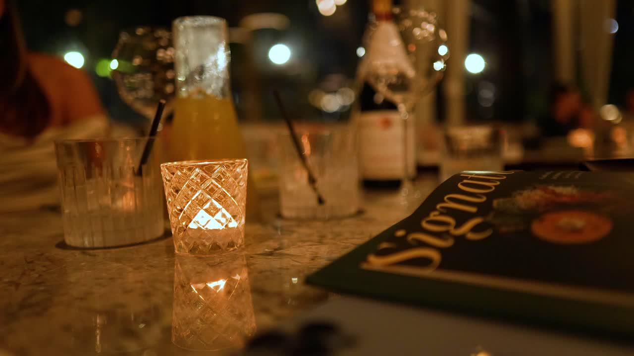 A cozy dinner setting with drinks, candlelight, and a hand gesturing, creating a warm, intimate atmosphere