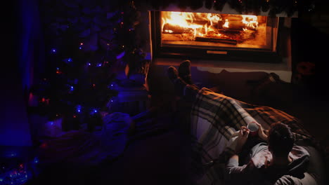 Young-Confident-Man-Resting-By-The-Fireplace-And-Christmas-Tree