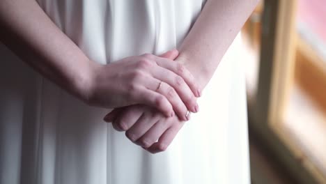 las manos de la mujer juntas delante de su vestido blanco