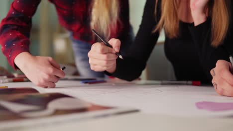 close up view of hands of young creative people drawing a draft with colored pencils on white sheets in the office during the