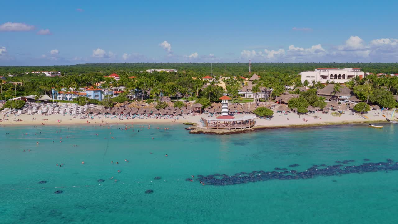 Vista aerea della città di Bayahibe con Dominicus Beach nella Repubblica Dominicana, con faro costiero, acque turchesi, bagnanti e costa fiancheggiata da palme lungo la vivace baia dei Caraibi. Scatto orbitale