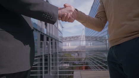 Successful-businessmen-shaking-hands-near-office-building