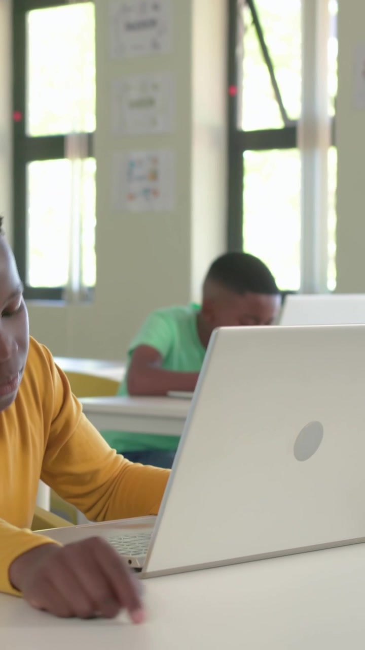 Vertical video: Appearing yellow peer causing green-tee and yellow-top boys using laptops for class