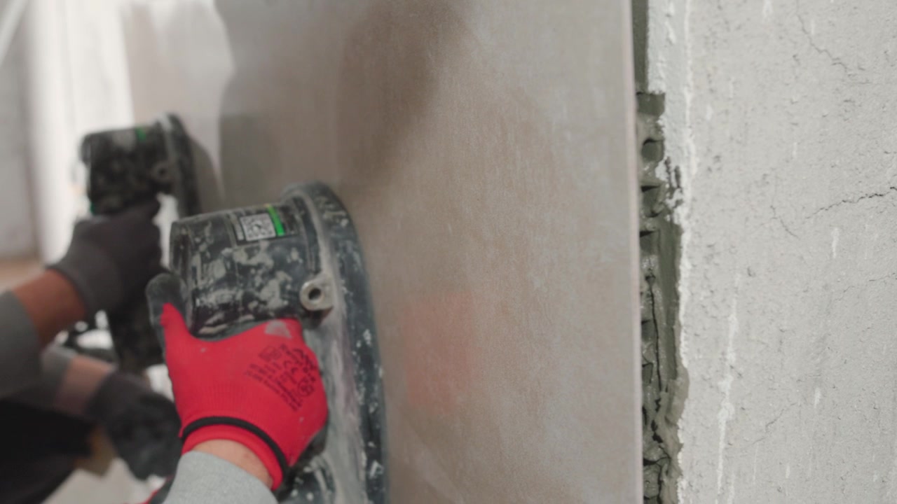 Installing a tile on the wall using hand vacuums. Professional contractor working on site.