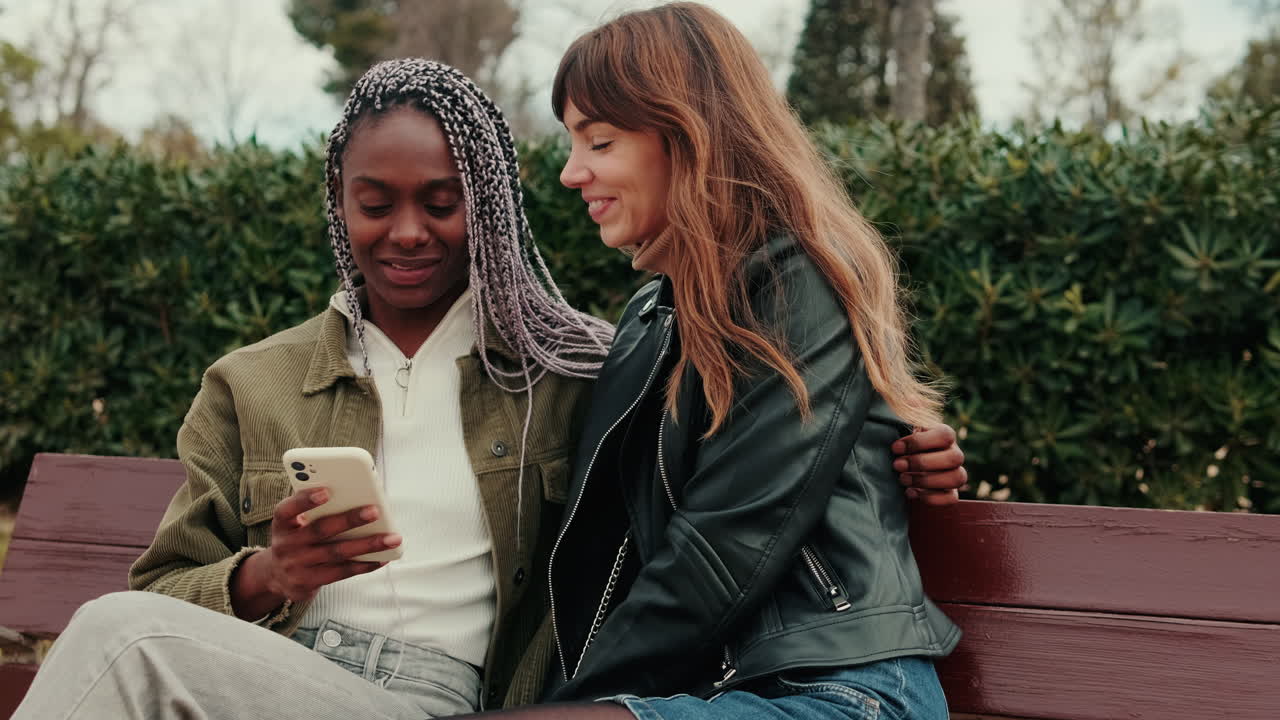 Glückliche junge Frauen teilen ein Smartphone auf einer Parkbank