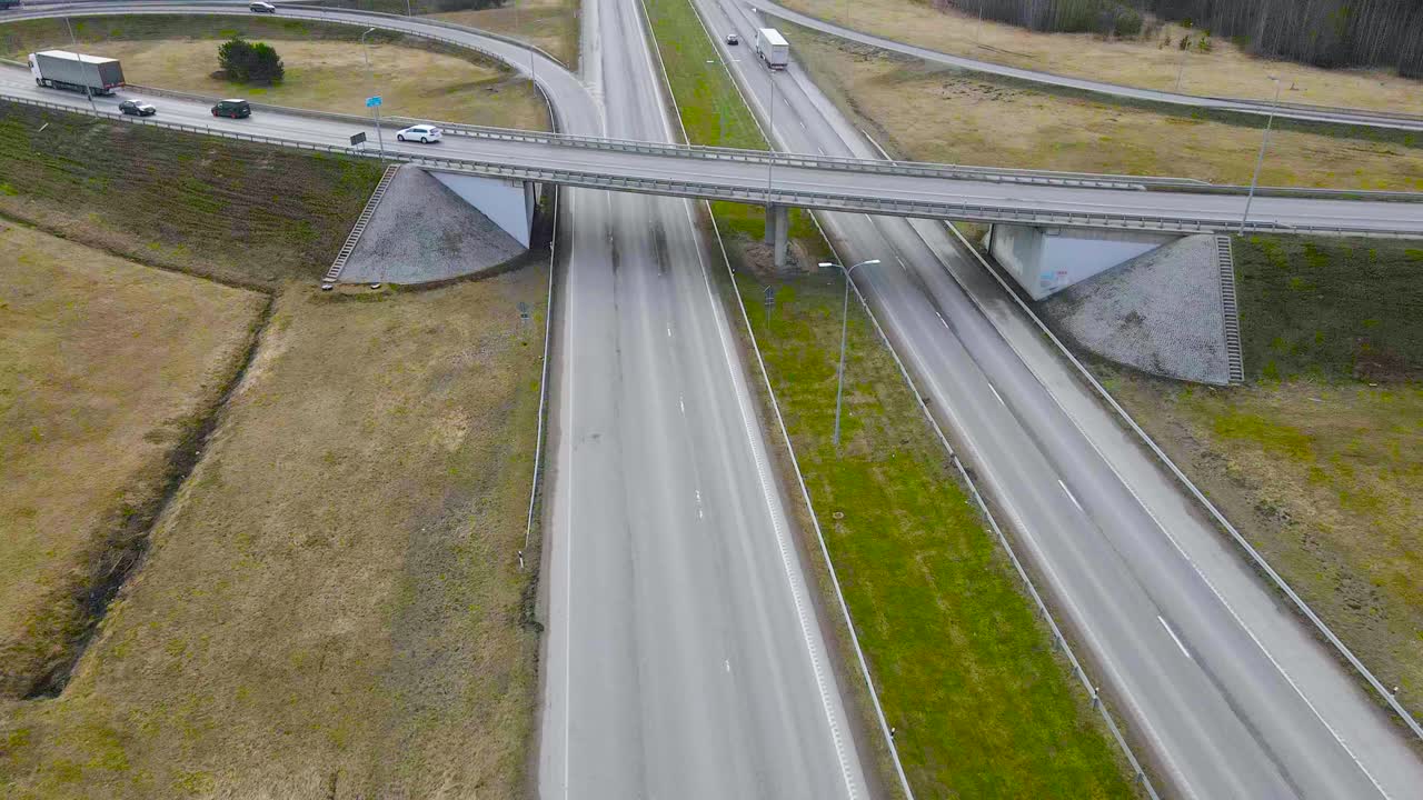 Aerial drone fotoage flying higher and revealing a large bridge overpass in Laagri Estonia going over Pärnu highway or Maantee during a cloudy spring or autumn day. Cars are driving on the road fast.