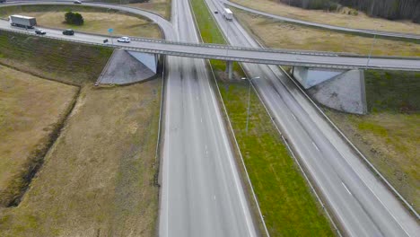 aerial drone fotoage flying higher and revealing a large bridge overpass in laagri estonia going over pärnu highway or maantee during a cloudy spring or autumn day. cars are driving on the road fast.