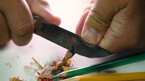 Footage-of-hands-slowly-sharpening-a-pencil-and-some-coloured-pencils-with-a-sharp-knife