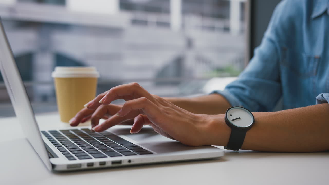 Close Up Of Businesswoman In Office Typing On Laptop Keyboard With Takeaway Drink In Background