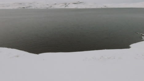 Snowy-ocean-shore-with-winter-mountains-in-background,-dolly-forward