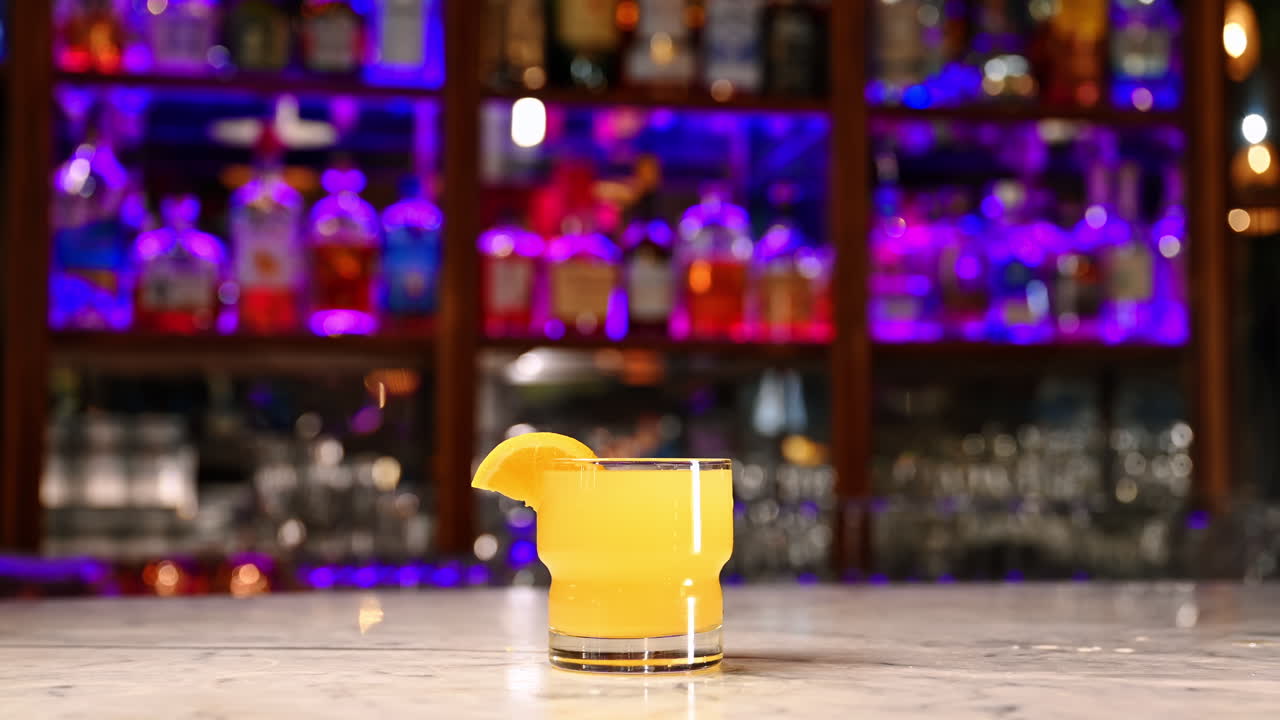 Cocktail giallo con fetta d'arancia in un bar moderno. Bicchiere basso di cocktail giallo con fetta d'arancia sul bancone sotto vivide luci al neon viola