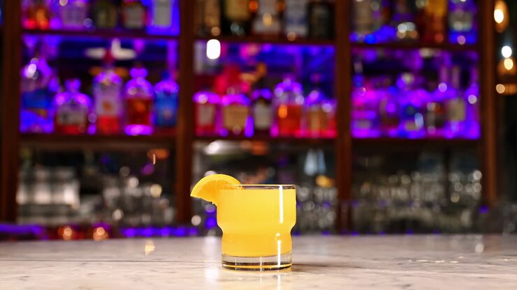 Cocktail giallo con fetta d'arancia in un bar moderno. Bicchiere basso di cocktail giallo con fetta d'arancia sul bancone sotto vivide luci al neon viola