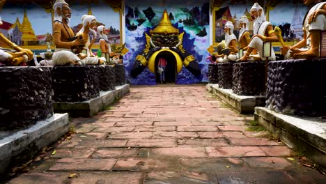 couple walking towards entrance at wat bang chak past seated statues. locked off