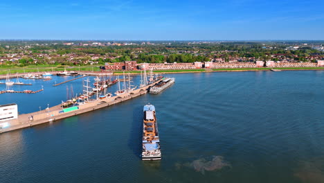 a barge heading to the port. aerial perspective on the marina of lelystad, the netherlands on sunny day. green cityscape at backdrop.
