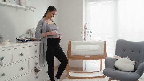 caucasian woman in advanced pregnancy standing in the baby's room next to the crib.