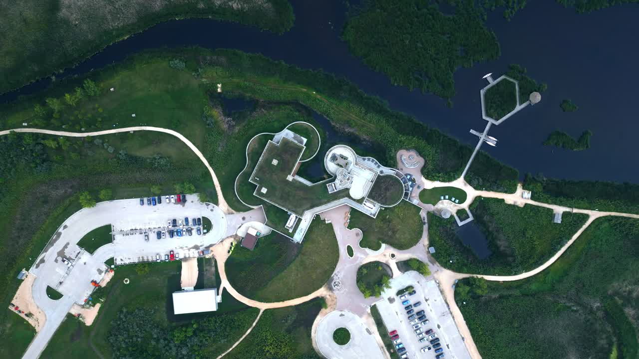 Drone ascends to reveal circular eco building and surrounding wetlands